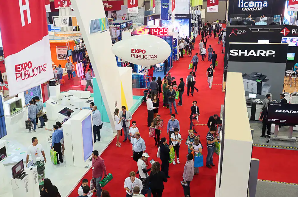 Vista aérea del piso de exhibición en ExpoPublicitas con stands, marcas patrocinadoras y asistentes recorriendo el evento de marketing y publicidad.